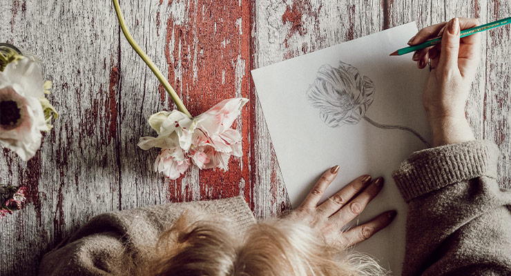 Draufsicht auf eine Frau, die auf einem Blatt Papier eine Blume zeichnet.