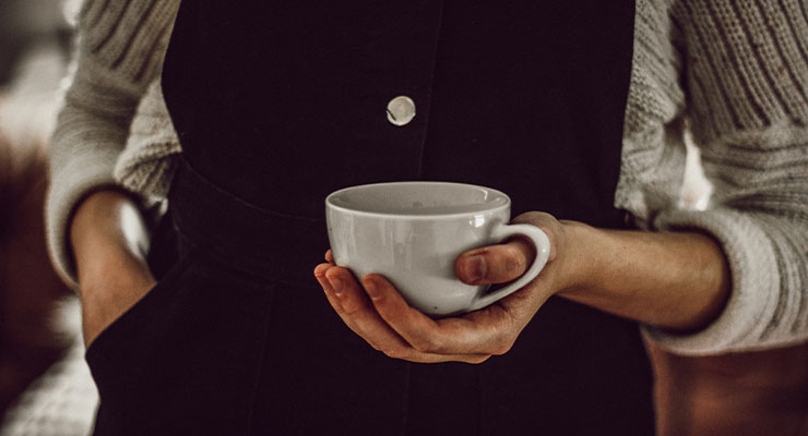 Frau mit kuscheligem Herbstoutfit und einer Tasse in der Hand