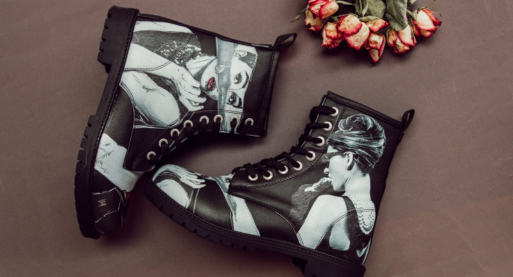 Schwarze Boots aus der DOGO Black Edition im Audrey Hepburn Design liegen auf grauer Pappe neben einem Strauß getrockneter Rosen.
