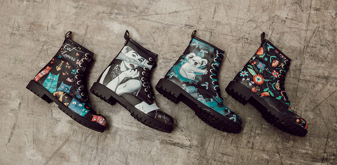 Vier schwarze Boots mit bunten Prints der Marke DOGO Shoes aus der limitierten DOGO Black Edition liegen auf einem grauen Hallenbode.